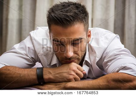 Sexy male model lying alone on his bed in his bedroom, looking at camera with a seductive attitude