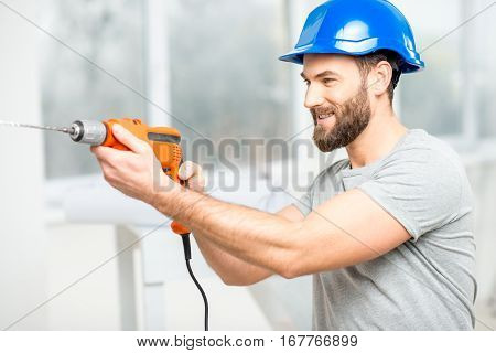 Handsome repairman in protective helmet drilling the wall indoors