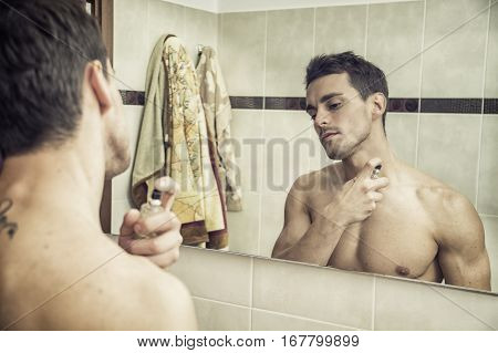 Handsome young man in his home bathroom, spraying cologne or perfume on neck