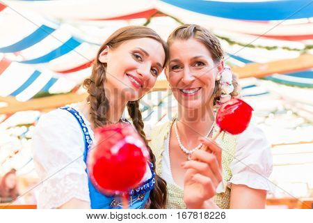 Two friends wearing dirndl and holding candy apples in a beer tent at Regensburger Dult