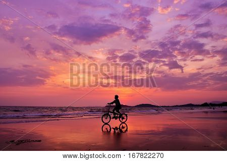 Silhouette of boy riding a bicycle on the beach with drametic sky
