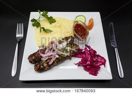 Lula kebab.Traditional Oriental dish, barbecue on fire shish kebab. Cutlets of lamb, onions, cabbage, mashed potatoes spicy tomato sauce with a fork and knife on a white plate . 