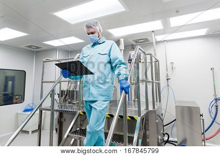 caucasian scientist in blue lab suit and gloves stand on steel ladder and check readings