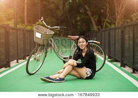 Pretty Thai girl sit near by bicycle at the park