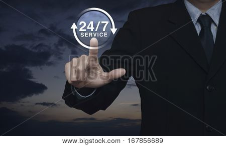 Businessman pressing button 24 hours service icon over sunset sky with clouds Full time service concept