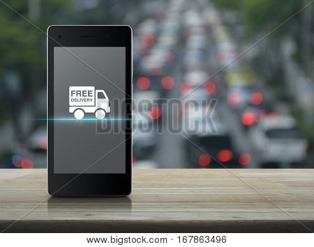 Free delivery truck icon on modern smart phone screen on wooden table over blur of rush hour with cars and road Transportation business concept