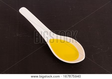 Olive oil presented in a ceramic spoon with a slate background macro.