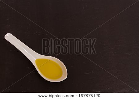 Olive oil presented in a ceramic spoon with a slate background macro.