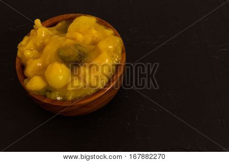 Piccalilli relish in a wooden bowl on a dark slate background.