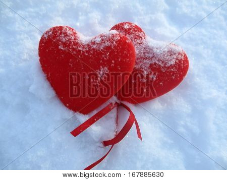 Red hearts with red ribbons in snow.