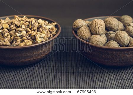 Walnut kernels and whole walnuts in brown ceramic bowls. Healthy organic food concept. Small debth of field