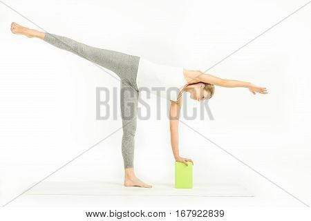 Sportswoman standing on yoga mat and doing Ardha Chandrasana posture Half Moon Pose with yoga block