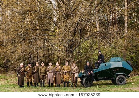 Pribor, Belarus - April 23, 2016: Unidentified Re-enactors Dressed As Russian Soviet Infantry Soldiers Of World War II Standing In Row At Armoured Soviet Scout Car BA-64 In Forest.