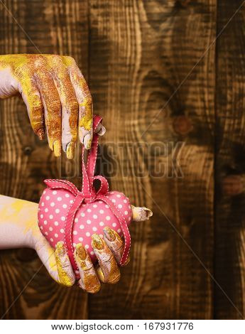 female hand smeared in golden paint or glister holding handmade pink polka dots valentine heart on brown vintage studio background selective focus