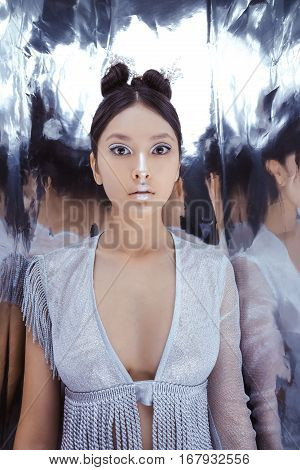 Portrait of futuristic scared young woman. Reflection of our mind and soul concept. Beautiful young multi-racial asian caucasian model cyber girl in silver urban clothes with conceptual hairstyle and make-up in metallik silver capsule.