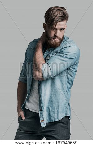 Perfect man. Young confident man looking at camera and holding hand on his neck while standing against grey background