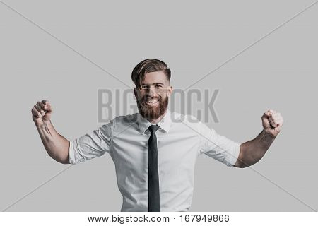 Feeling so happy! Handsome young businessman gesturing and smiling while standing against grey background