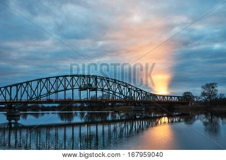 Steel bridge over the river. The light piercing through the clouds.