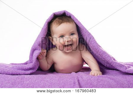 Newborn baby lying down and smiling in a purple towel.