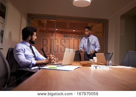 Businessman stands talking to work colleague late in office