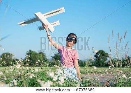 Asian Girl Dressed As Pilot Playing Airplane Toy At Grass Flower Paddy Field.