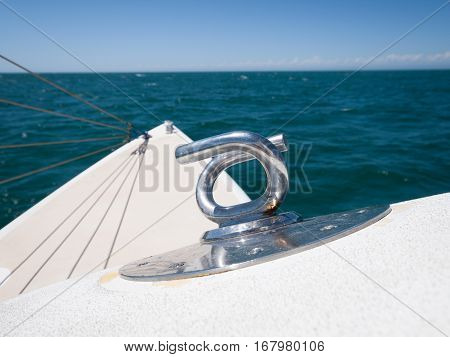 Metal rope anchor point on a yacht boat with a green sea and blue sky backdrop