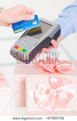 Wireless payment terminal with credit or debit card at shop with gifts in the background 