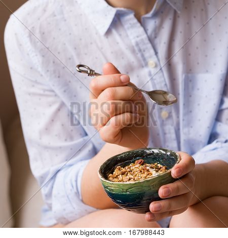 Young woman with muesli bowl. Girl eating breakfast cereals with nuts pumpkin seeds oats and yogurt in bowl. Girl holding homemade granola. Healthy snack or breakfst in the morning.