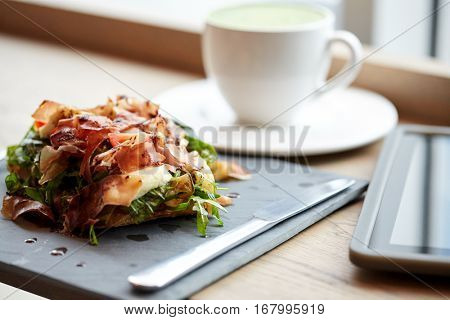 food, dinner, haute cuisine and eating concept - prosciutto ham salad on stone plate with tablet pc and drink at restaurant