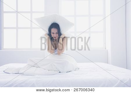 Young caucasian woman covering her head and ears with pillows.