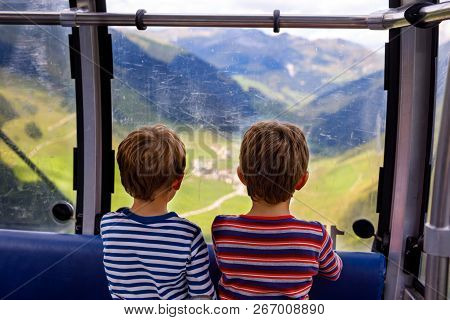 Two Little Boys Sitting Inside Of Cabin Of Cable Car And Looking On Mountains Landscape.