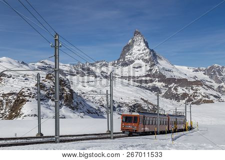 Zermatt, Switzerland - April 12, 2017: The Red Gornergrat Train In Front Of The Snowy Matterhorn Mou