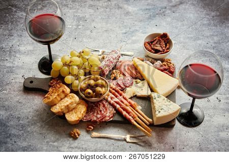 Antipasto platter cold meat and cheese board with grapes, wine, various kinds of cheese, grissini bread sticks on white rustic background. View from above