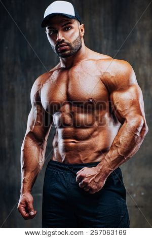 Young strong man bodybuilder in cap on stone wall background