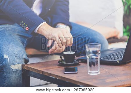 Close Up Of Businessman Hand Stirring A Cup Of Coffee With Tablespoon In Cafe.
