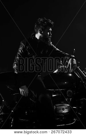 Man With Beard, Biker In Leather Jacket Lean On Motor Bike In Darkness, Black Background. Brutality 