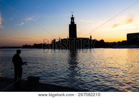 Silhouette Of Fisherman With Fishing Pole And Stockholm City Hall Stadshuset Building Municipal Coun