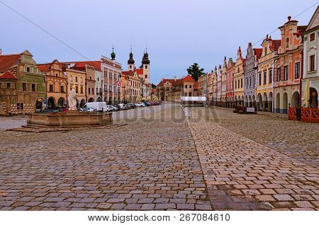 Morning Landscape Of Main Square In Telc. Fountain With Statue Of St. Margaret, Towers Of Holy Name 