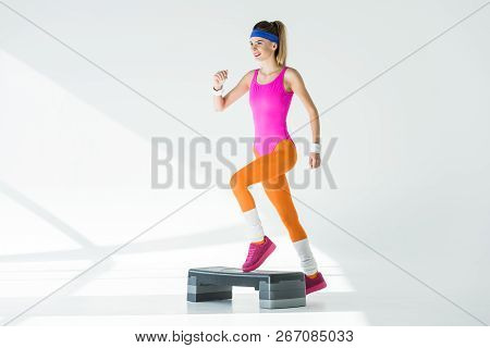 Smiling Sporty Woman Exercising On Step Platform And Looking Away On Grey