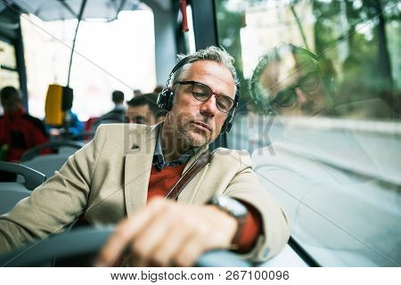 Mature Tired Businessman With Heaphones Travelling By Bus In City.