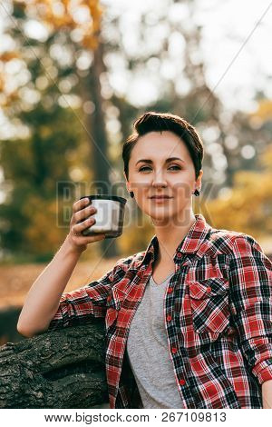 Adult Woman Looking At Camera Hoding Metallic Thermos Cup On Blurred Autumnal Background