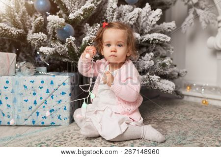 A Little Girl Is Playing With A Garland With A New Year Tree. Danger. Disobedient Child. Good New Ye