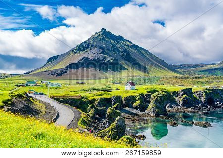 View Of The Basalt Rocks Formation On The Coastline With The Beautiful Houses And The Mountain Stapa