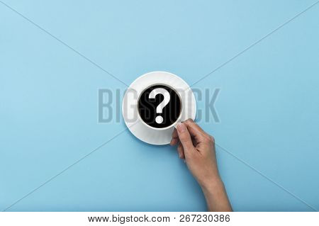 Female Hand Holding A White Cup With Black Coffee On A Blue Background. Question Mark. Flat Lay, Top
