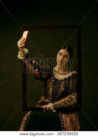 Portrait Of A Girl Wearing A Princess Or Countess Dress With Mobile Phone Over Dark Studio Making Se