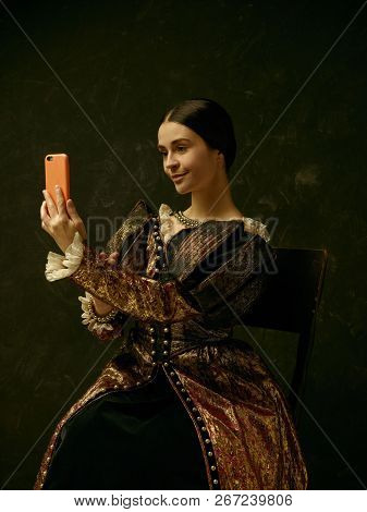 Portrait Of A Girl Wearing A Princess Or Countess Dress With Mobile Phone Over Dark Studio Making Se