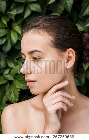 Thoughtful Young Woman With Hand Near Face And Green Leaves At Background