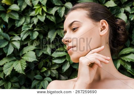 Thoughtful Young Woman With Hand Near Face And Green Leaves At Background