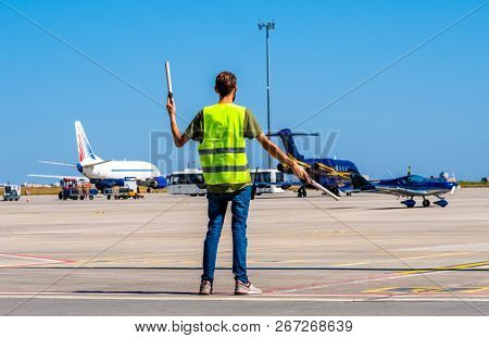 Dispatcher geaturing signs directing the blue shiny sport plane on the airport runway