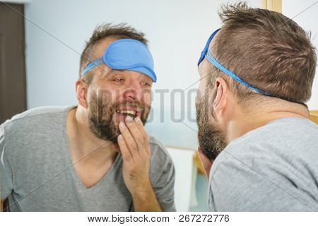 Adult Man With Eyemask On His Forehead Feeling Fresh After Waking Up, Looking At Himself In Bathroom